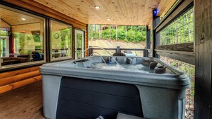 Eine Holzhütte mit Whirlpool, großen Fenstern und Blick auf den Wald.