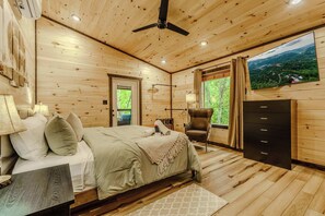 A wooden-paneled bedroom with a bed, a chair, a dresser, and a TV on the wall. - New Build 2B-2B Cabin With Hot Tub & Sauna (Sevierville)