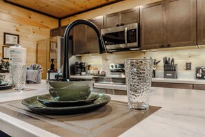 A kitchen with wooden cabinets, a stainless steel microwave, and a water dispenser. - New Build 2B-2B Cabin With Hot Tub & Sauna (Sevierville)