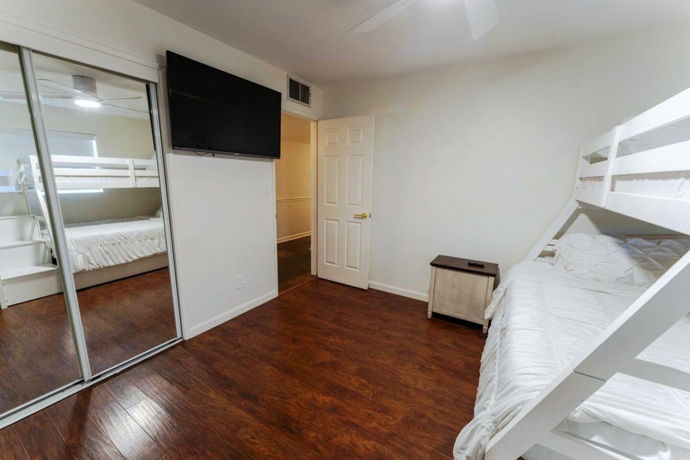 Ein Schlafzimmer mit Etagenbett, Schiebetürenschrank, Fernseher und einem kleinen Nachttisch.