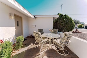 A patio with a round table and four chairs, a door, and a small garden area with plants and a rock feature. - Private Pool + Detached Bunkhouse | Sleeps 10 (Scottsdale)