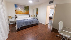 Un dormitorio con cama, escritorio, silla, ventilador de techo y un cuadro en la pared.