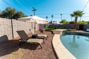 A backyard with a swimming pool, two lounge chairs, a small table, and a covered patio area. - Walk to Old Town Pool + Bunkhouse | Sleeps 8 (Scottsdale)
