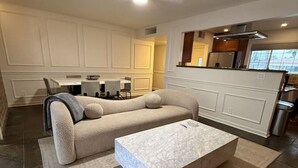 Una sala de estar moderna con un sofá modular, una mesa de centro y una zona de cocina con armarios y un refrigerador.