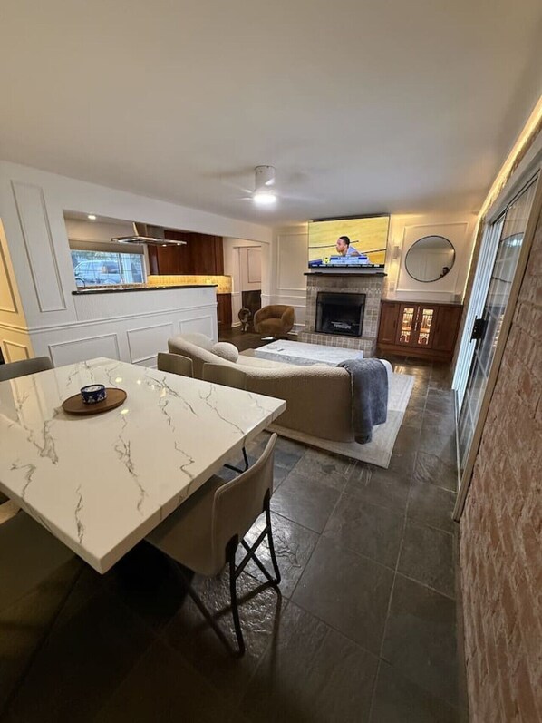 A modern living room with a fireplace, a dining area with a marble table, and a kitchen with wooden cabinets. - Walk to Old Town Pool + Bunkhouse | Sleeps 8 (Scottsdale)