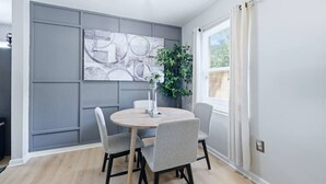 A dining area with a round table, four chairs, a wall-mounted abstract painting, a potted plant, and a window with curtains. - Ice Bath, Fire Pit & Outdoor Bar · 3BR House · Uptown Charlotte (Charlotte)