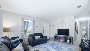 A living room with a dark sofa, a TV, and a fireplace. - Ice Bath, Fire Pit & Outdoor Bar · 3BR House · Uptown Charlotte (Charlotte)
