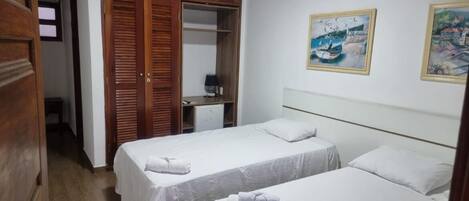 A hotel room with two beds, wooden wardrobe, and artwork on the wall.