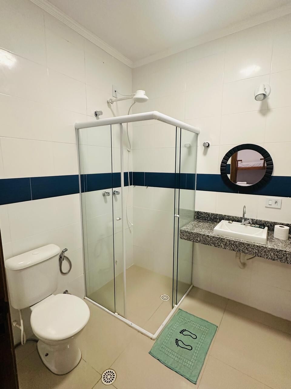 Ein Badezimmer mit einer Duschkabine, einer Toilette, einem Waschbecken mit Marmorplatte und einem Spiegel.
