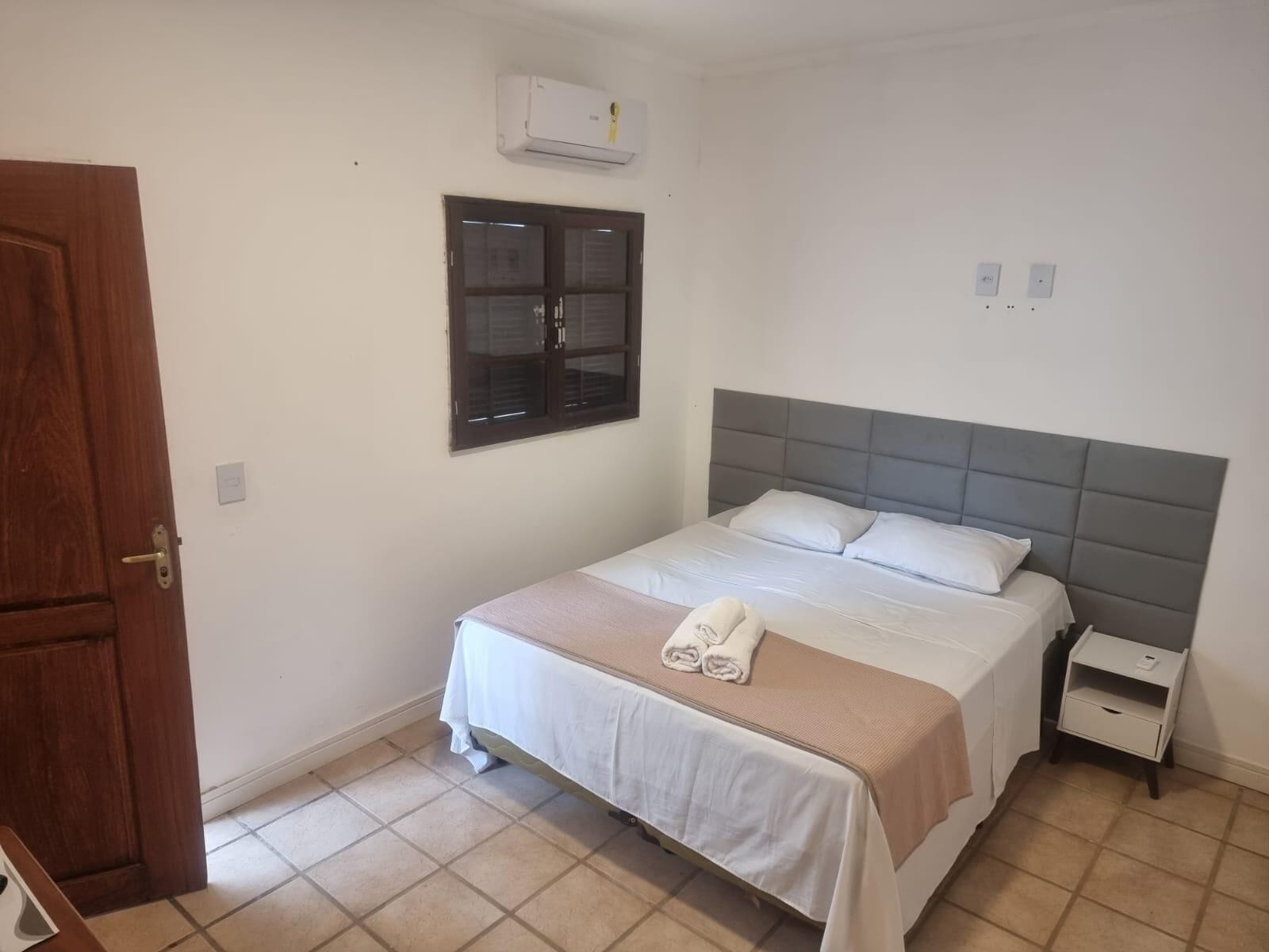 A bedroom with a bed, a nightstand, a window, and an air conditioning unit.