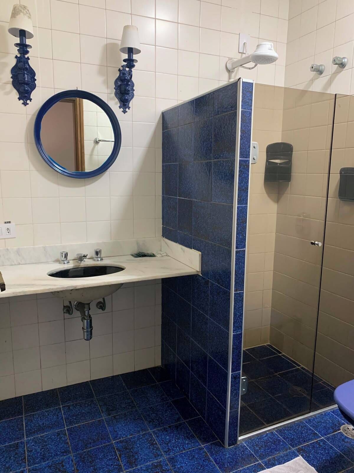 Un baño con lavamanos, espejo, cabina de ducha con azulejos azules y puerta de cristal.