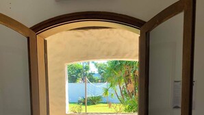 A hotel room with an open doorway leading to a balcony with a view of greenery and a pool. - Pousada Villa Novo Tempo (Guarujá)