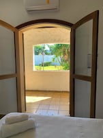 Quarto de hotel com porta aberta para varanda, vista para área verde e piscina.