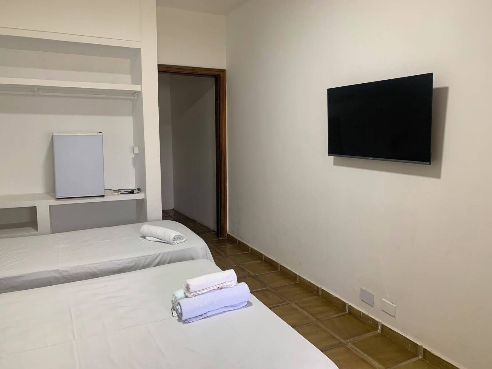 A hotel room with two beds, a TV, a refrigerator, and a door leading to another room.