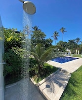Piscina sob um céu azul límpido, rodeada por vegetação exuberante e palmeiras.