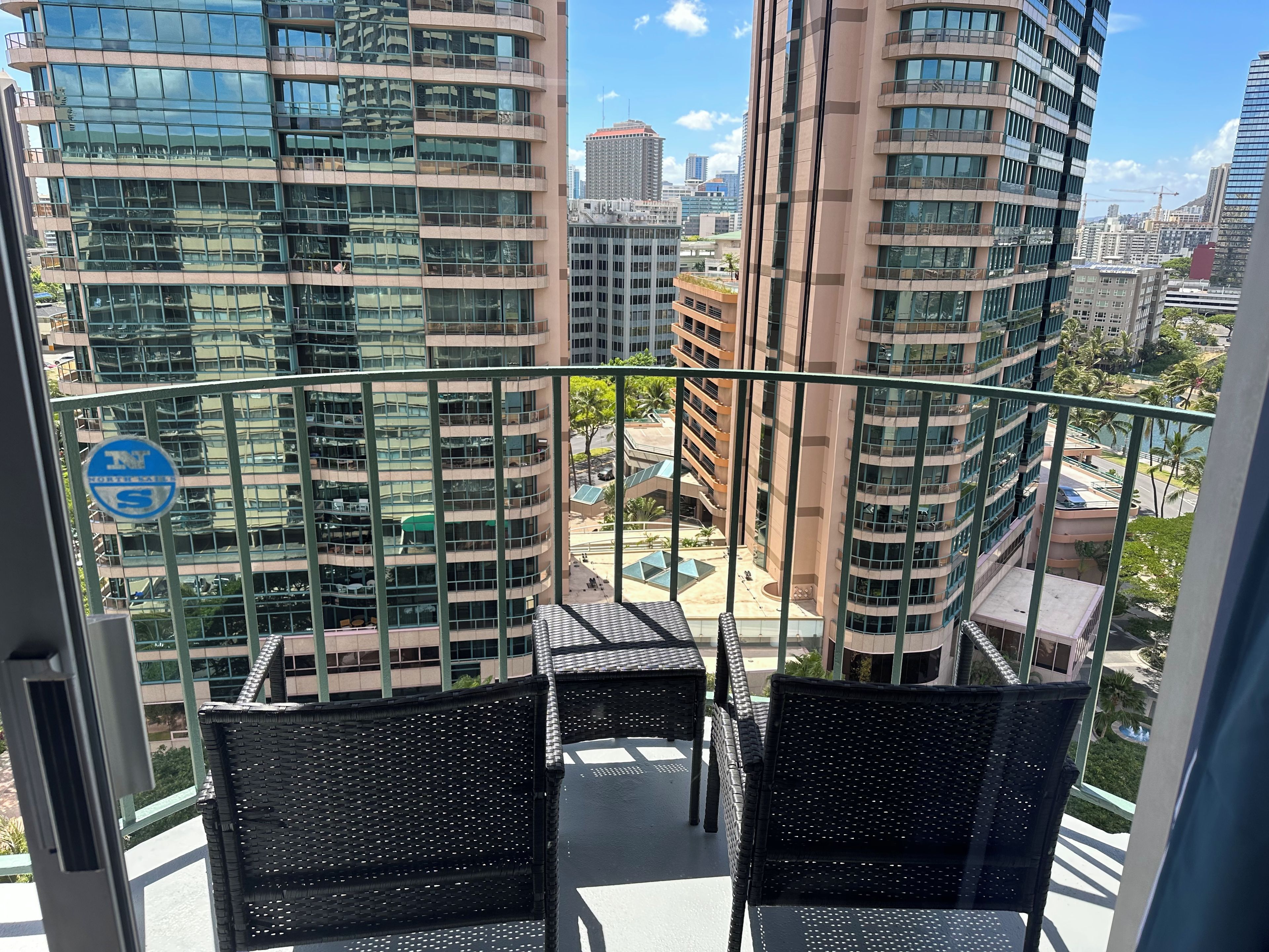 Un balcon doté de meubles en osier, offrant une vue sur un paysage urbain avec de nombreux immeubles de grande hauteur.