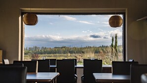 A dining area with tables and chairs, a large window with a view of a forest and sky.