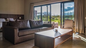 A modern hotel room with a large window, a sofa, a coffee table, and a chair.