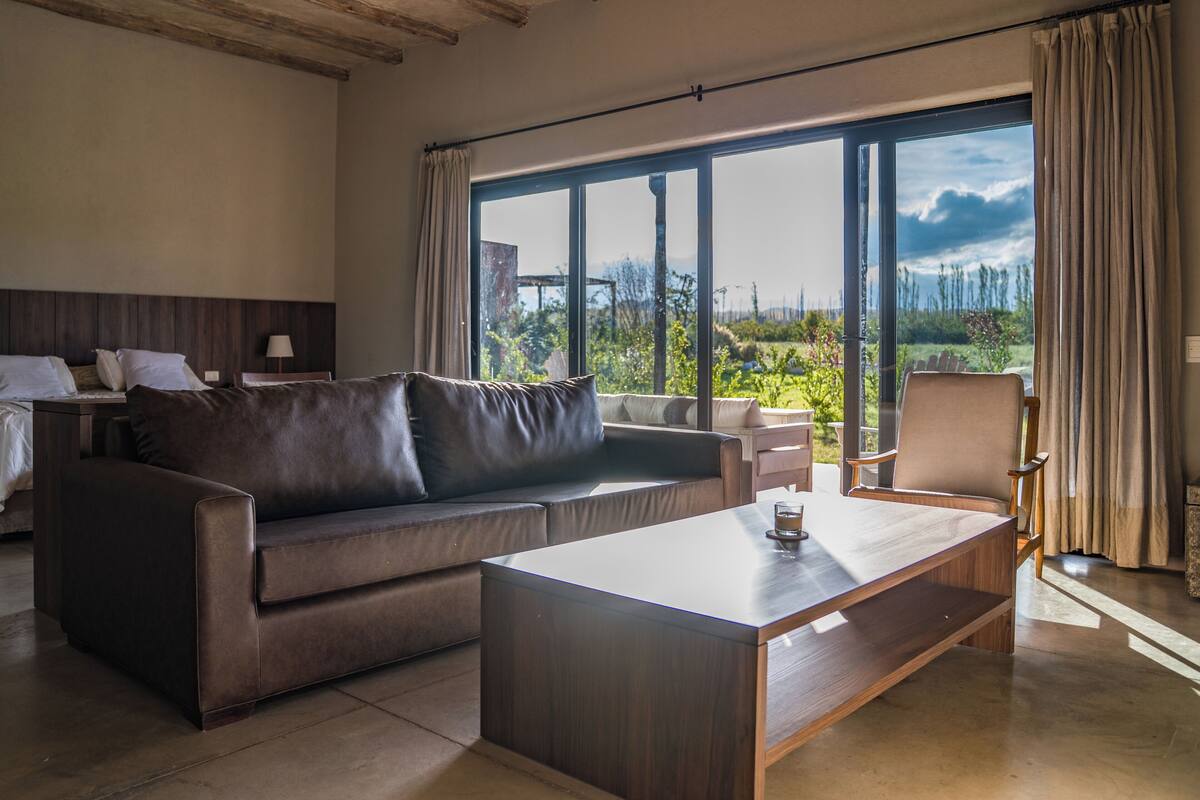 A modern hotel room with a large window, a sofa, a coffee table, and a chair.