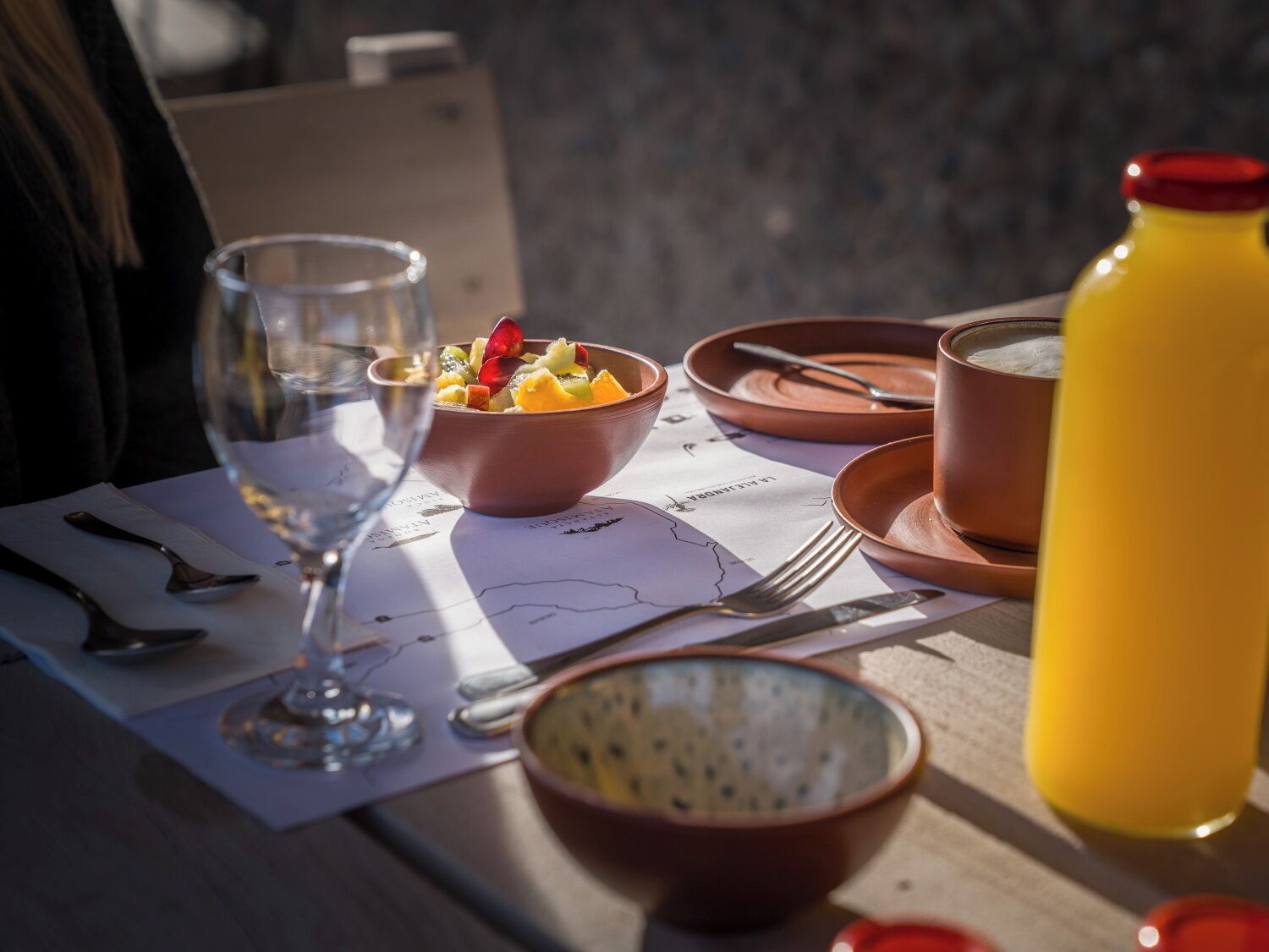 Taula preparada amb un plat de fruita, un got d'aigua, un got de suc i una tassa, amb un mapa damunt la taula.