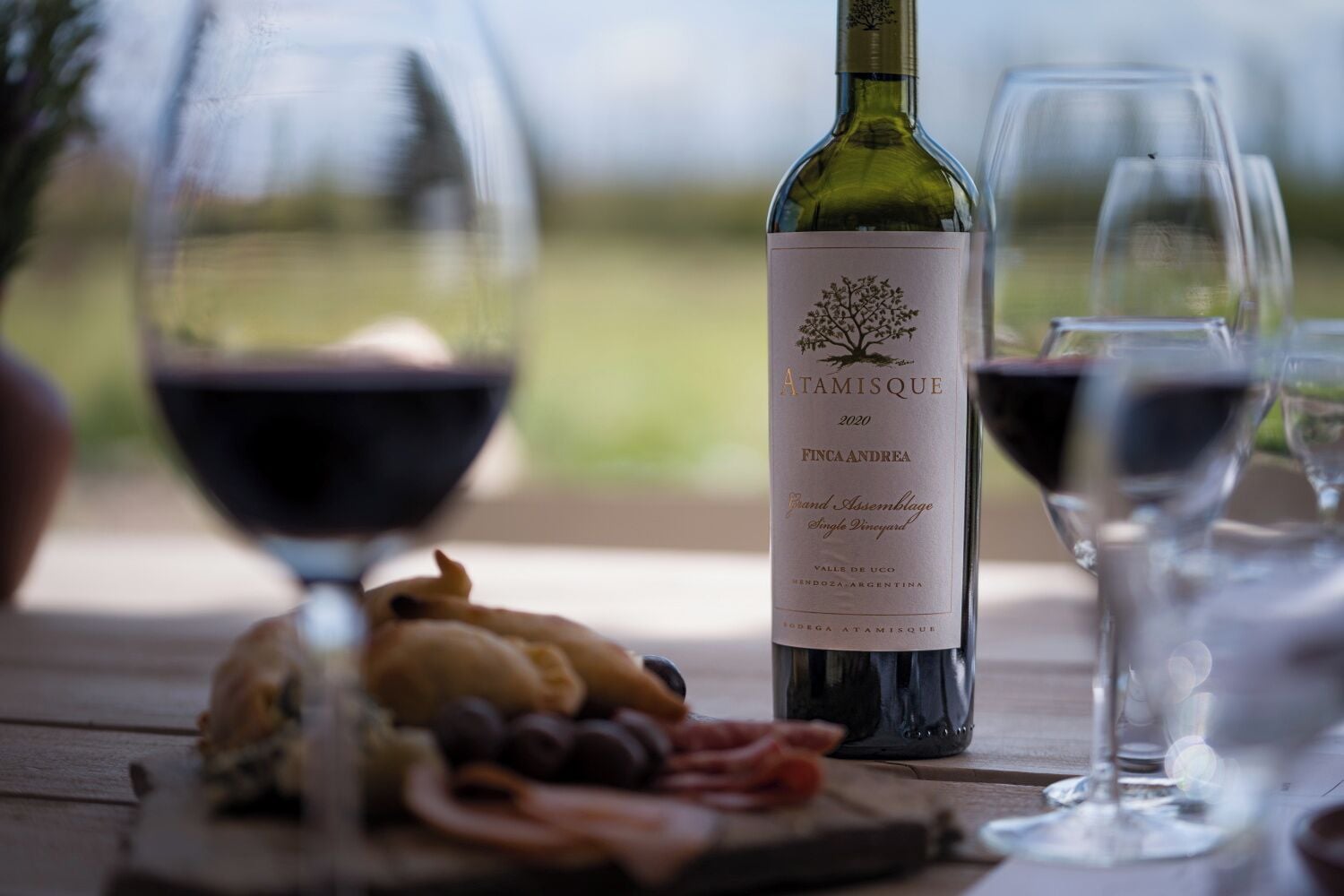 Une bouteille de vin avec une étiquette, un verre de vin rouge et une assiette remplie de divers aliments, le tout posé sur une table en bois.