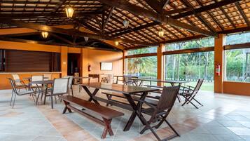 An outdoor dining area with wooden tables and chairs, a covered roof, and large windows.