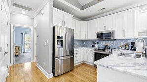 A modern kitchen with white cabinets, stainless steel appliances, a marble countertop, and a blue-tiled backsplash. - 4BR NMB Ocean Drive Cottage, quiet community and walk to everything you need! (North Myrtle Beach)
