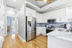 A modern kitchen with white cabinets, stainless steel appliances, a marble countertop, and a blue-tiled backsplash. - 4BR NMB Ocean Drive Cottage, quiet community and walk to everything you need! (North Myrtle Beach)
