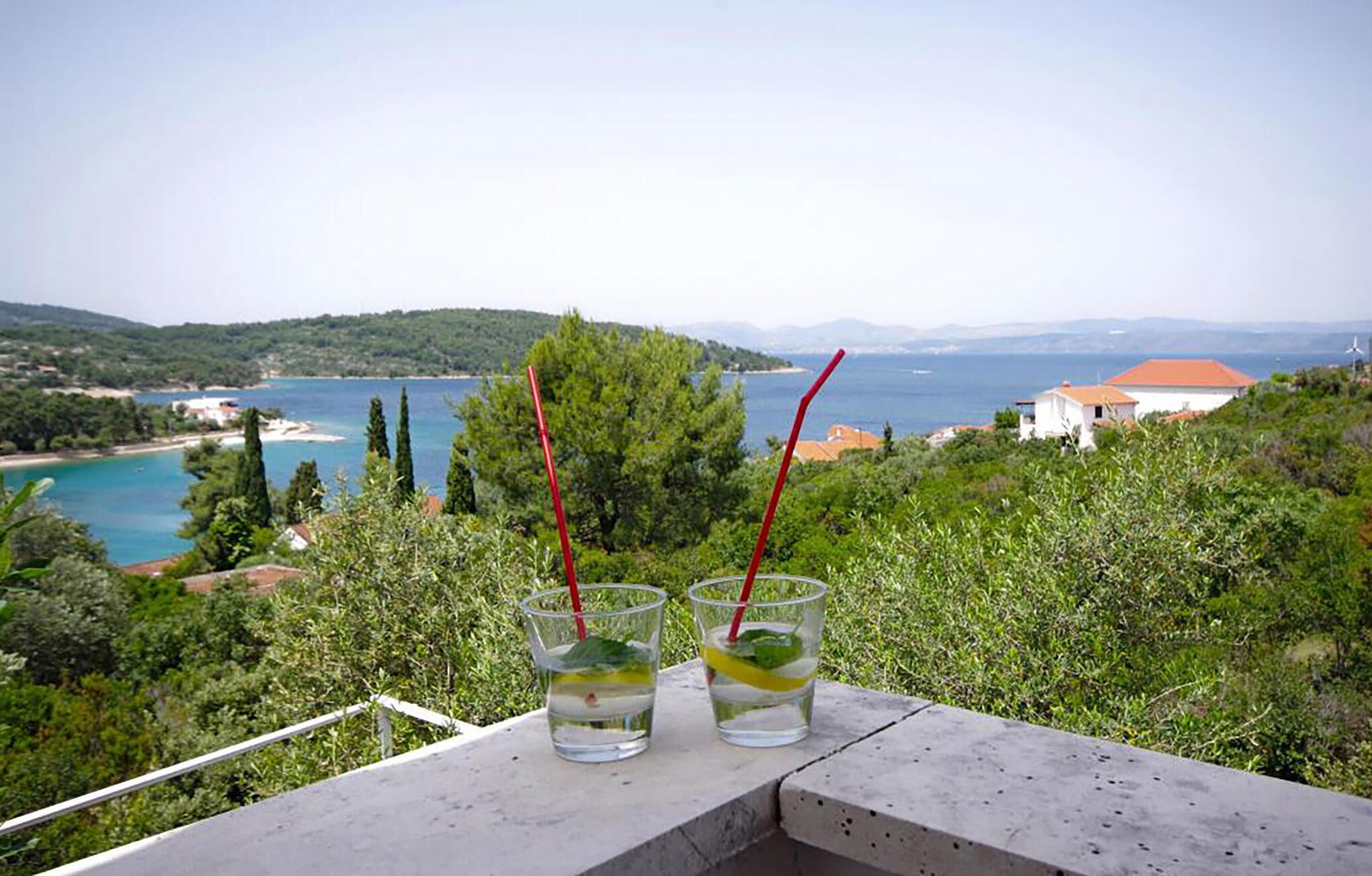 Dos vasos de una bebida con pajita en un balcón con vistas a un paisaje costero.