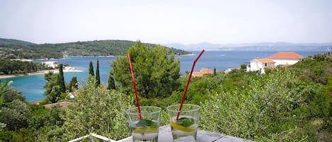 Dos vasos de una bebida con pajita en un balcón con vistas a un paisaje costero.