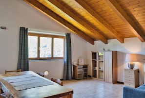 A room with a wooden ceiling, a dining table with chairs, a cabinet, and a window with curtains.