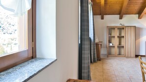 Une pièce avec une fenêtre, des poutres apparentes en bois au plafond, une armoire et un sol carrelé.