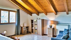 Une pièce avec un plafond en bois incliné, une fenêtre avec des rideaux, un meuble, un radiateur et un canapé bleu.