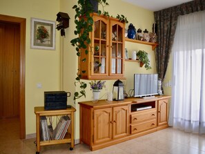 A living room with a wooden cabinet, a television, a plant, and a small table with a radio. - R166 Apartment 50m from the sea with two swimming pools (Calafell)