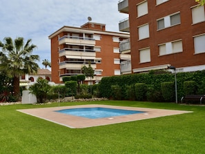 A residential building with a swimming pool surrounded by well-maintained grass and palm trees. - R166 Apartment 50m from the sea with two swimming pools (Calafell)