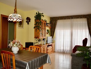 A dining area with a table, chairs, a chandelier, a television, and a cabinet with plants. - R166 Apartment 50m from the sea with two swimming pools (Calafell)