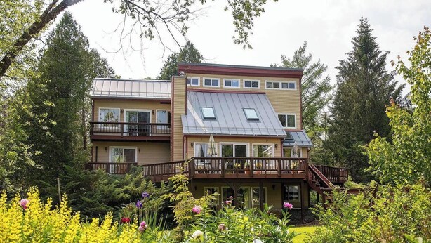 Ein zweistöckiges Haus mit Balkon, einer überdachten Terrasse und einem Garten mit verschiedenen Pflanzen und Blumen.