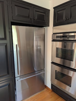 Eine Küche mit Edelstahl-Kühlschrank und -Ofen, schwarzen Schränken und Holzboden.