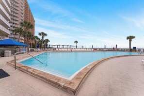 A swimming pool with a blue water feature, surrounded by palm trees and a tall building. - Dunes of Panama 2BR / 2BA Beachfront Condo C401 (Panama City Beach)