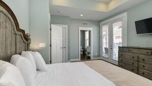 Un dormitorio con una cama grande, un aparador, un televisor y un baño visible a través de una puerta abierta.