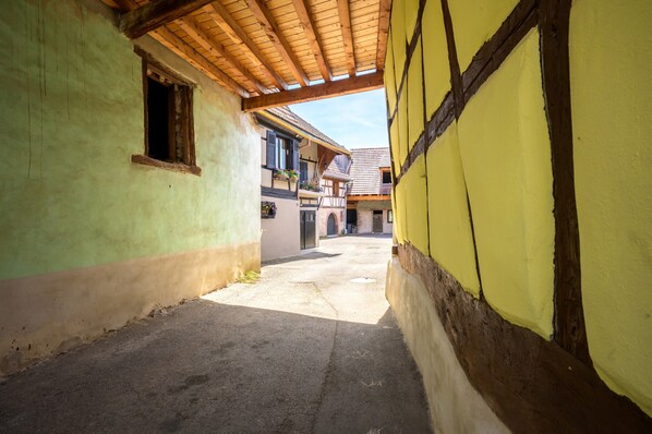A narrow alleyway between buildings with a wooden ceiling and a clear sky.