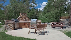 Un espace barbecue extérieur doté de murs en pierre, d’une table et de chaises.