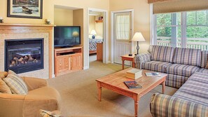 A living room with a fireplace, sofa, television, and a view through a window. - Vermont Mountain Escape Near Skiing with Spacious 2BR Deluxe Retreat (Cambridge)