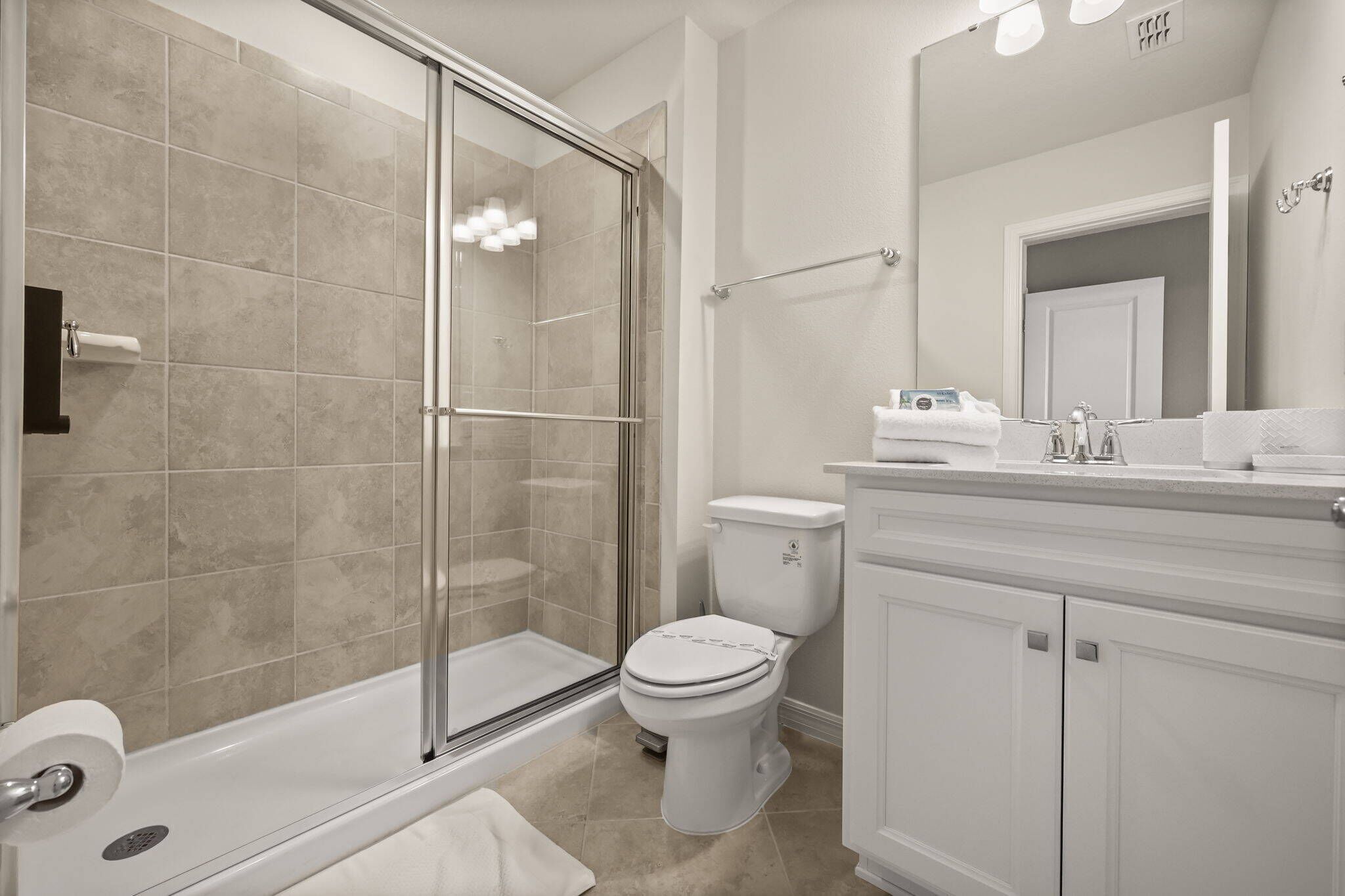 Un baño moderno con cabina de ducha de vidrio, inodoro y tocador con espejo.
