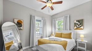 Un dormitorio con cama, mesita de noche, espejo y ventilador de techo.