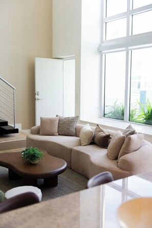 A modern living room with a sectional sofa, a coffee table, and a view of greenery outside. - Modern Loft in the Rosemary District-DT Sarasota 2 (Sarasota)