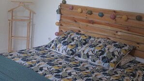 A bedroom with a wooden bed, a hanging rattan light fixture, a wooden headboard, and two wall art pieces.
