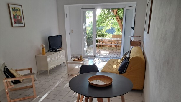 A living room with a sofa, a dining table, a TV, and a sliding glass door leading to an outdoor patio.