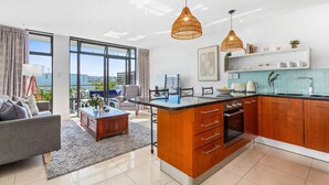 A modern kitchen with a central island, wooden cabinets, and a large window offering a view of the city. - Eden On The Bay 174B (Cape Town)