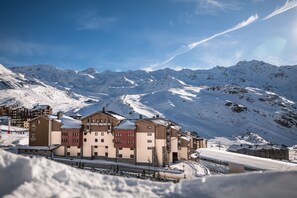 A snow-covered mountain resort with multiple buildings, including a hotel with a ski lift visible in the background.